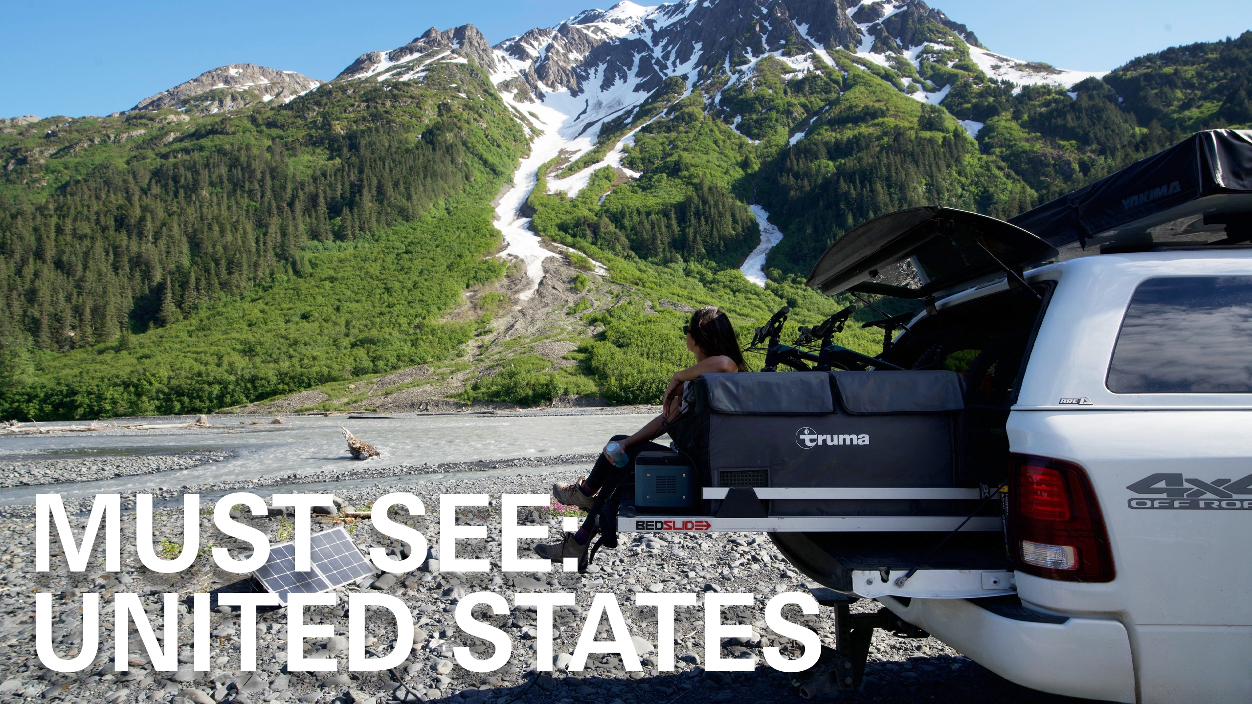 Woman sitting on truck bed in front of snowy mountain