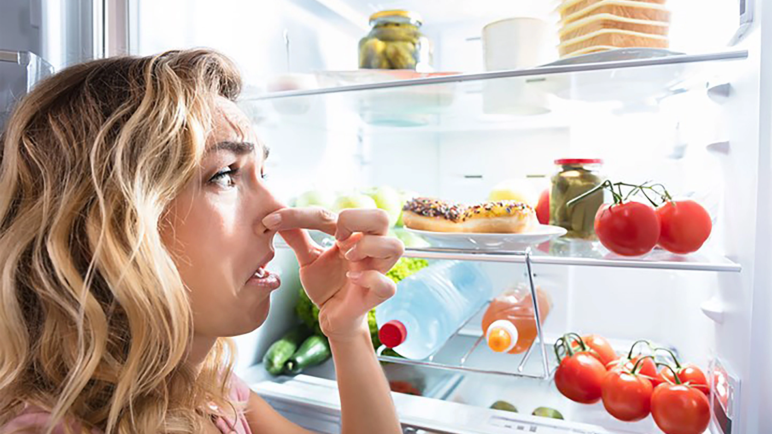 woman holding nose in front of fridge
