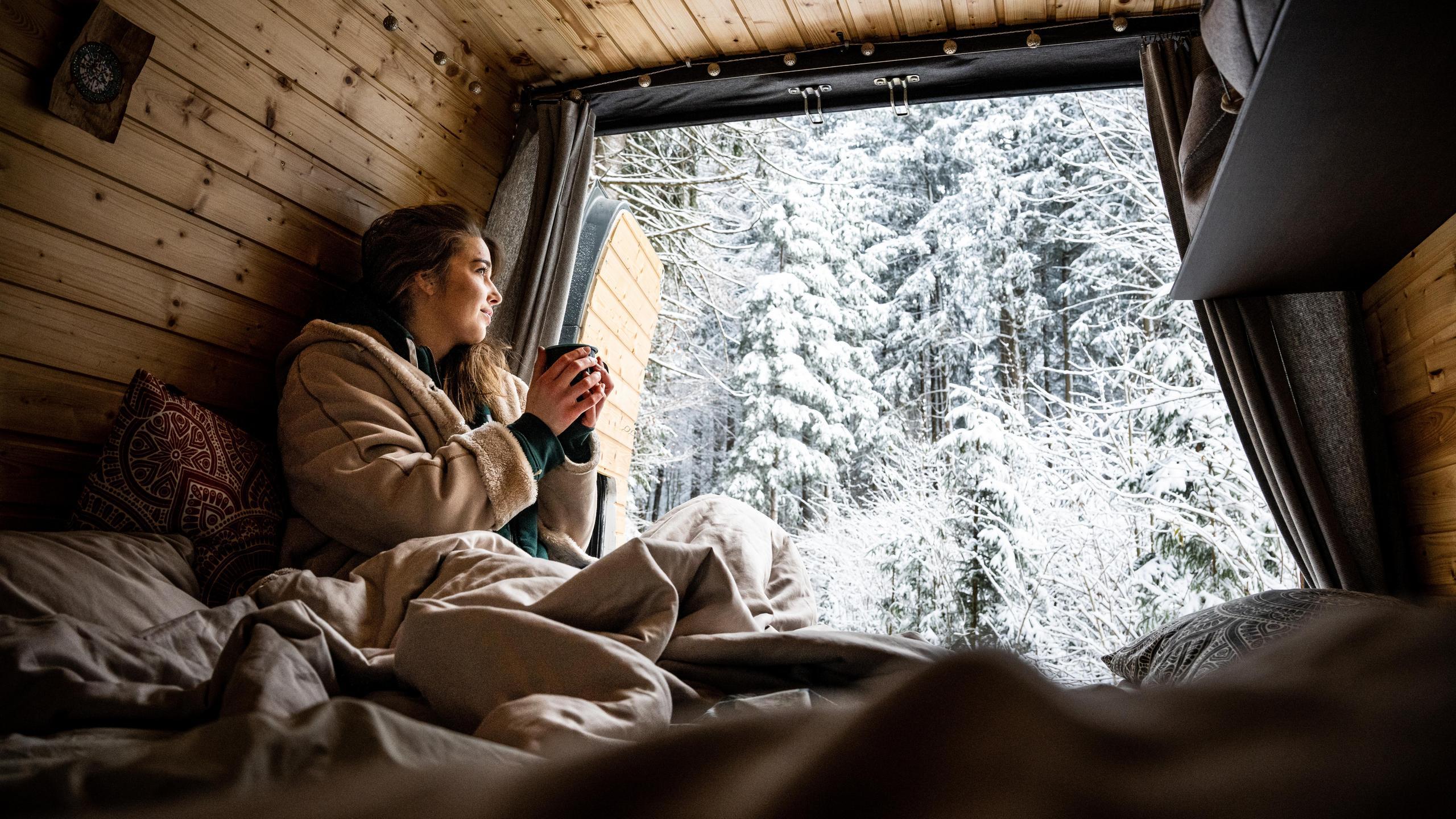 View from the tailgate of a motorhome over a snowy winter landscape, woman with cup